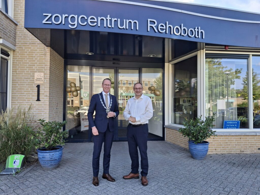 Twee heren, waaronder een burgemeester, voor de ingang van zorgcentrum Rehoboth