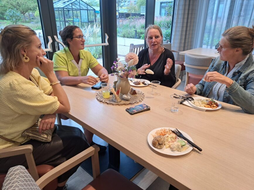 Een paar vrouwen zitten aan tafel met elkaar te eten en te praten