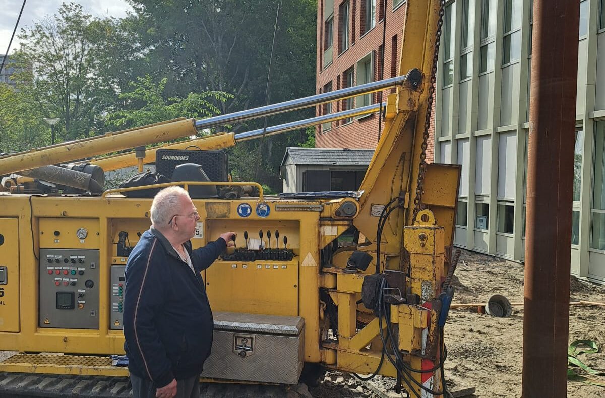 Een oudere man staat naast een heimachine