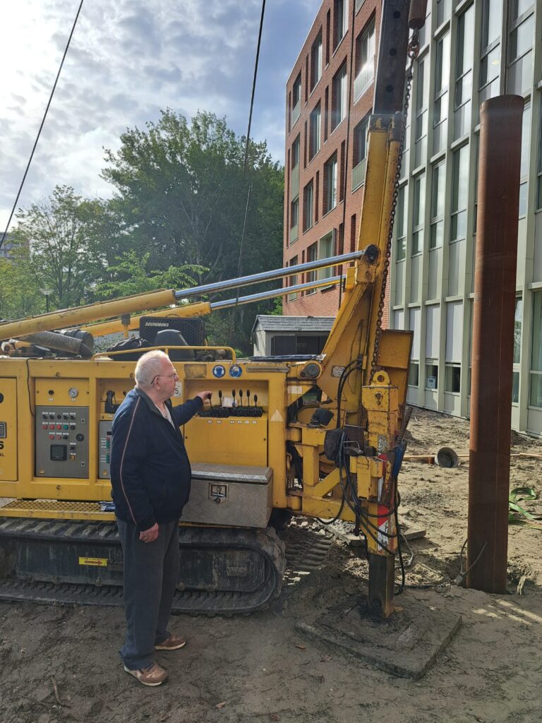 Een oudere man staat naast een heimachine